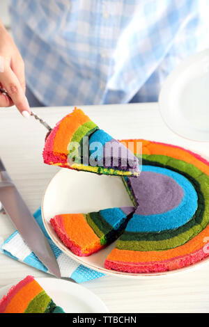 Giovane donna di taglio torta arcobaleno in cucina Foto Stock