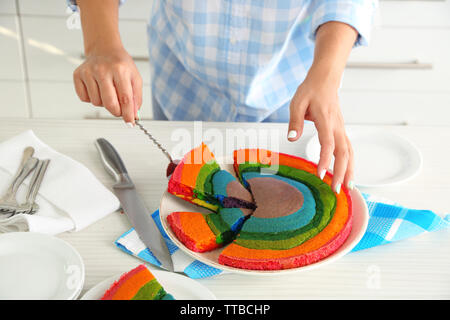 Giovane donna di taglio torta arcobaleno in cucina Foto Stock