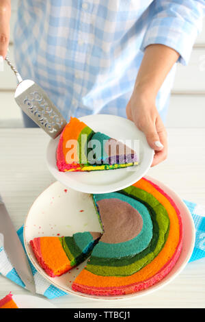 Giovane donna di taglio torta arcobaleno in cucina Foto Stock