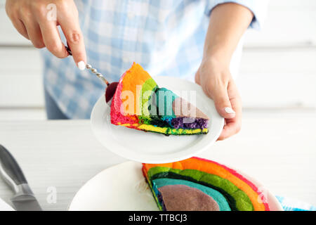 Giovane donna di taglio torta arcobaleno in cucina Foto Stock