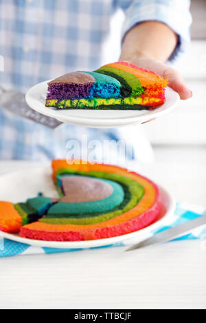 Giovane donna tenendo la piastra con la porzione di rainbow torta in cucina Foto Stock