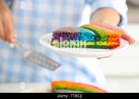 Giovane donna tenendo la piastra con la porzione di rainbow torta in cucina Foto Stock