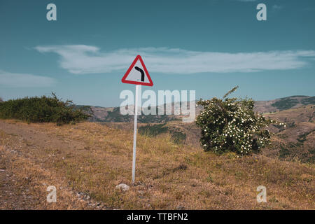 Cartello stradale pericoloso, girare a sinistra, all'aperto, montagna, cielo blu, vuoto. Foto Stock