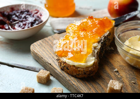 Gustose marmellate nella ciotola, burro, pane fresco e tablet sul blu sullo sfondo di legno Foto Stock