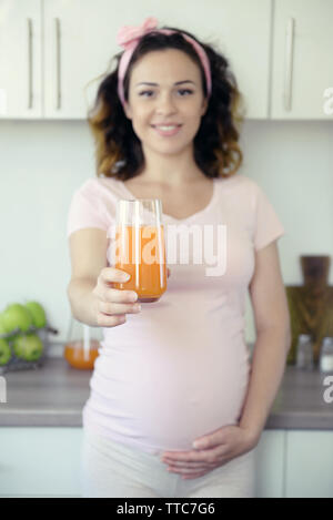 Felice giovane donna incinta con un bicchiere di succo di frutta sulla cucina Foto Stock