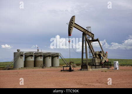 Martinetto pompa olio grezzo e serbatoi di stoccaggio di produzione con un Cielo nuvoloso nel bacino di Powder River del Wyoming Foto Stock