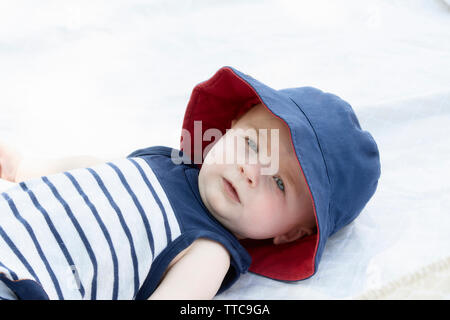 Blue-eyed Baby Boy sdraiato sulla schiena fuori su una coperta con il cappello per la protezione solare Foto Stock