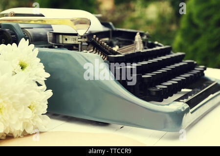 Vintage macchina da scrivere nero con documenti e fiori sul tavolo di legno, all'aperto Foto Stock