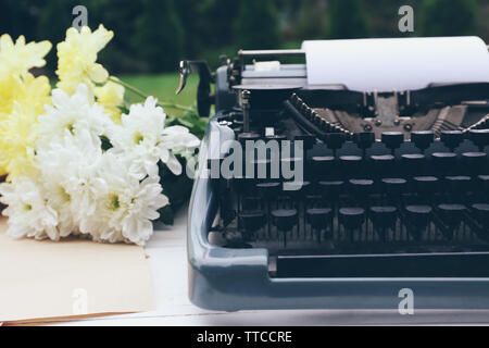 Vintage macchina da scrivere nero con documenti e fiori sul tavolo di legno, all'aperto Foto Stock