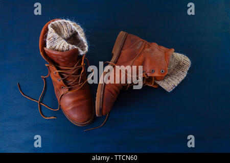 Vecchio rosso sporco scarpe alte su sfondo blu. Vecchia scuola vintage indossato scarpe con lacci in cuoio e maglia di lana warm grey calzini. Foto Stock