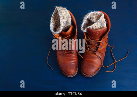 Vecchio rosso sporco scarpe alte su sfondo blu. Vecchia scuola vintage indossato scarpe con lacci in cuoio e maglia di lana warm grey calzini. Foto Stock