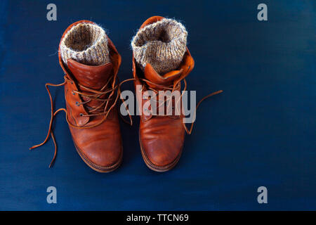 Vecchio rosso sporco scarpe alte su sfondo blu. Vecchia scuola vintage indossato scarpe con lacci in cuoio e maglia di lana warm grey calzini. Foto Stock