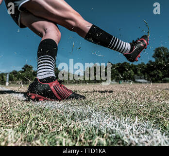 Un giovane giocatore di calcio lascia uno spruzzo di erba sospesi in aria dopo calci ad un pallone da calcio Foto Stock