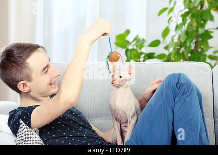 Giovane uomo bello sedersi con cat sul lettino a casa Foto Stock