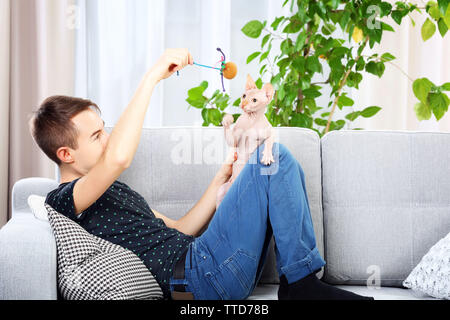 Giovane uomo bello sedersi con cat sul lettino a casa Foto Stock