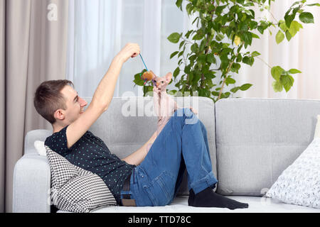 Giovane uomo bello sedersi con cat sul lettino a casa Foto Stock