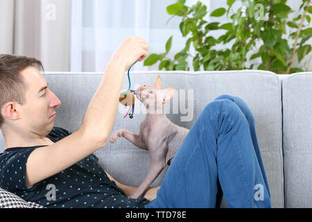 Giovane uomo bello sedersi con cat sul lettino a casa Foto Stock