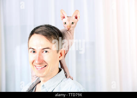 Giovane uomo bello tenendo un gatto sulla luce sullo sfondo di tulle Foto Stock