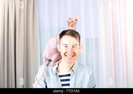 Giovane uomo bello tenendo un gatto sulla luce sullo sfondo di tulle Foto Stock