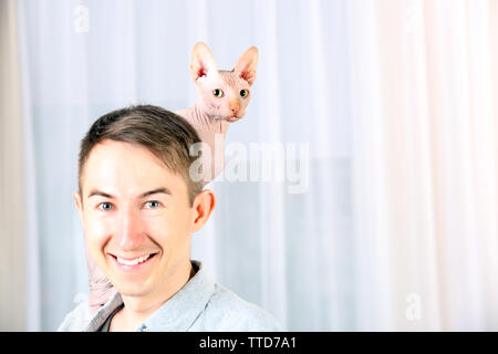 Giovane uomo bello tenendo un gatto sulla luce sullo sfondo di tulle Foto Stock