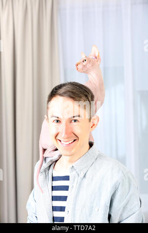 Giovane uomo bello tenendo un gatto sulla luce sullo sfondo di tulle Foto Stock