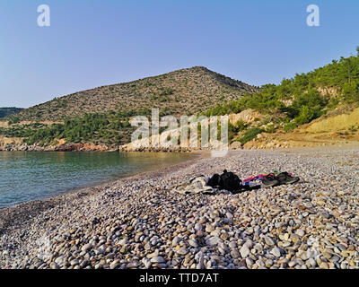 Vuota isolata in pietra bellissima spiaggia di estate, nella zona centrale di West Chios Island, Grecia, nuotatore vestiti, borsa e asciugamano. Foto Stock