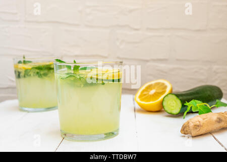 Due bicchieri di acqua Sassy con ingredienti (cetriolo, zenzero, foglie di menta, limone) su bianco sullo sfondo di legno con spazio di copia Foto Stock