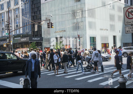 I pedoni attraversano il sempre occupato angolo della Quinta Avenue e la 57th Street nel centro di Manhattan. Foto Stock