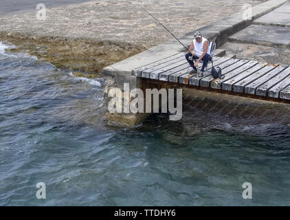 SANTA PONSA, MALLORCA, Spagna - 29 Maggio 2019: rilassato pescatore seduto su un ponte di legno dall'acqua su 29 Maggio 2019 a Santa Ponsa, Mallorca, Spagna Foto Stock