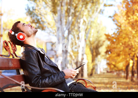 Giovane uomo seduto su una panchina nel parco e ascolto di musica Foto Stock