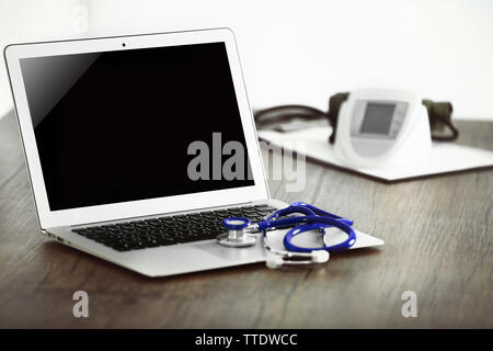 Computer portatile con uno stetoscopio e sangue misuratore di pressione sul tavolo di legno in office Foto Stock