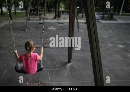 Ragazza giovane oscillanti in un parco giochi per bambini senza nessuno attorno a. Foto Stock