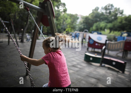 Ragazza giovane oscillanti in un parco giochi per bambini senza nessuno attorno a. Foto Stock