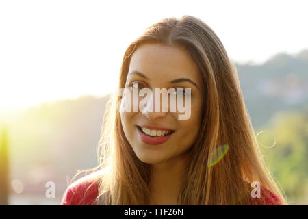 Close-up ritratto di giovane e bella donna adulta nella luce del sole al tramonto. Bella ragazza sorridente. Bella donna sta godendo di caldo e la luce del sole. Foto Stock