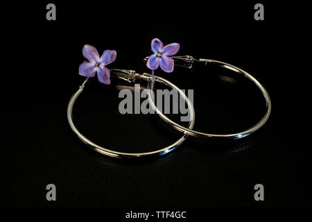 Brillante rotondo di metallo sottile orecchini e fiori lilla su uno sfondo nero. Foto Stock