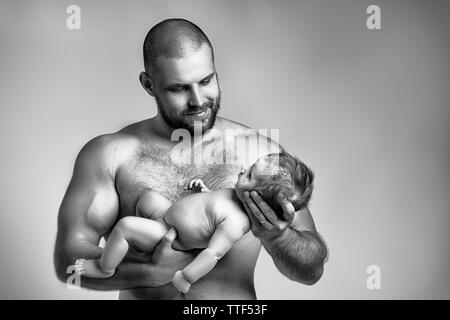 Ritratto di un neonato ragazzo, di età di 1 mese, capelli rossi, occhi blu, che papà tiene nelle sue braccia, strettamente coccole e sorrisi. Il concetto di famiglia, LOV Foto Stock