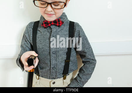 Ragazzo vestito come uomo anziano guarda verso il basso in corrispondenza della canna da zucchero indossando occhiali Foto Stock