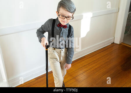 Bambino vestito come ingrigimento vecchio uomo pretende di camminare con la canna da zucchero Foto Stock