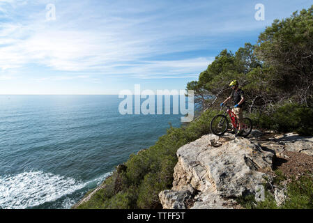 Mountainbiker permanente sulla parte superiore delle rocce, si affaccia sul mare. Foto Stock