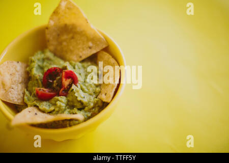 Close-up del guacamole con tortilla chips servito in tazza su sfondo giallo Foto Stock