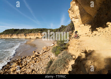 Ciclista in sella a una moto su un percorso attraverso la parete di pietra arenaria vicino al mare Foto Stock