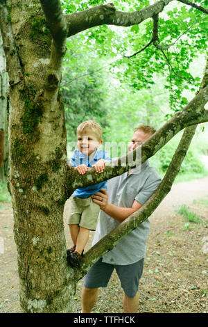 Dritto in vista di un papà aiutando il suo giovane figlio salire un albero Foto Stock