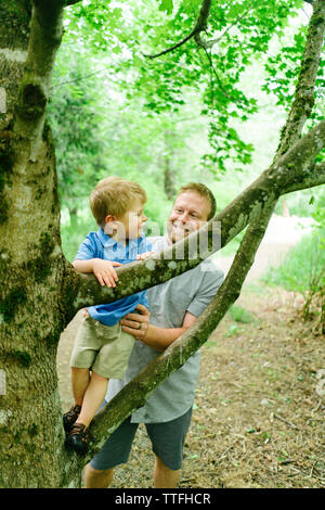 Dritto in vista di un papà aiutando il suo giovane figlio salire un albero Foto Stock