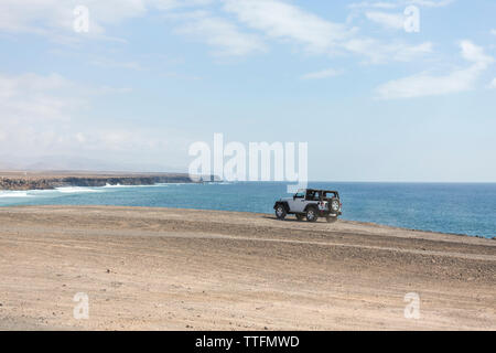 Bianco jeep 4x4 la guida su una scogliera oceaniche con ocean in background Foto Stock