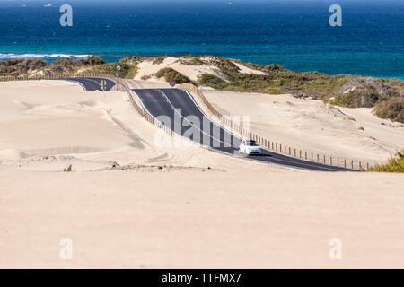 Bianco auto guida su strada asfaltata nel deserto con Sfondo oceano Foto Stock