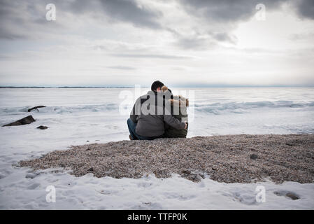 Giovane seduti insieme sul lago ghiacciato sulla riva di un nuvoloso giorno d'inverno. Foto Stock