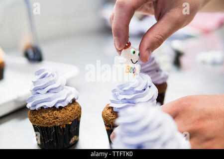 Mano del pasticciere aggiungere un dolce zucchero ghost su un cupcake di halloween Foto Stock