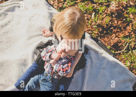 Suor trattiene il suo fratello mentre sulla coperta picnic al di fuori in posizione di parcheggio Foto Stock