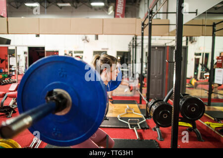 Vista laterale della bella donna facendo un barbell squat in studio fitness Foto Stock