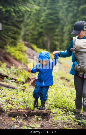 Vista ritagliata della madre aiutare suo figlio toddler equilibrio su un log. Foto Stock